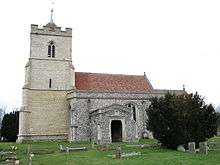 A stone church seen from the south with a red tiled roof showing, from the left, a relatively large embattled tower, then the south aisle with a porch