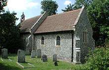 A simple small flint church with a red tiled roof and a bellcote at the far end