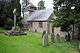 A square base of three stone steps supporting a mounting block and crucifix, also of stone, in the churchyard of a small church