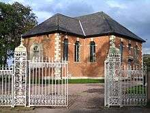 Small brick Neoclassical chapel behind ornate iron gates