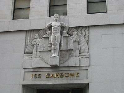 A color photograph of a nude male figure carved in stone over the entrance of a commercial building. The figure stands straight with arms akimbo and hands atop a stone disc behind the figure, flanked by geometric designs and two smaller figures of workmen looking off to each side. Below the sculpture grouping, raised gold letters read "155 Sansome".