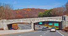 A stone bridge over a divided highway in an autumn landscape