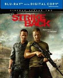 A blu-ray disc cover with a textured background and the title "Strike Back" in red letters on the top with the subtitle "Diplomacy is overrated" in white letters below. Below it are two men. The man on the left is stubbly with a blue shirt and holding a machine gun in his right hand. The man on the right is wearing a green T-shirt and holding a machine gun with both hands. Behind them is what appears to be smoke and buildings of some sort.