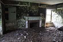View of the interior of an abandoned house with peeling walls and a floor that is buried under a deep layer of soil
