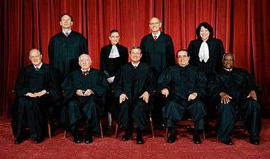 Nine judges in black robes pose for a photograph, five are seated, four stand behind them.