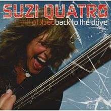 The front cover of Suzi Quatro's album Back to the Drive. Quatro is in close-up, with only her head and one of her shoulders visible. She is screaming while playing a bass guitar, with graphics that make the cover appear to be a window that she has shattered. One of her eyes is closed; the other is covered by her hair. She is wearing a black leather jacket and a silver necklace with a silver heart on it. Behind her is a light blue background.