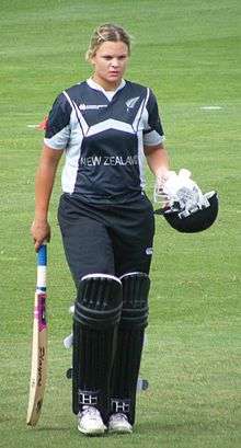 A female New Zealand cricketer, in a black uniform, holding a bat in her right hand and a helmet in her left hand