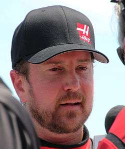 A man in his mid-thirties; he has a full beard and wears a black baseball cap with a red logo.