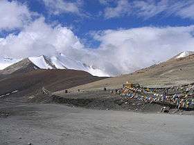 Gravel road through high mountains with brightly coloured prayer flags at the side