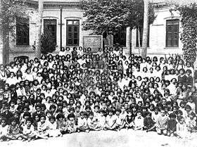 A black-and-white photograph of several dozen girls seated in front of a school building