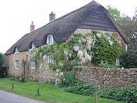 Thatched house with wisteria growing up the near end.