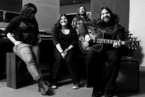 A black-and-white photo of The Magic Numbers leaning and sitting