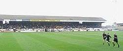 A colour photograph of a typical English lower-league grandstand, marked "Cambridge United Football Club"