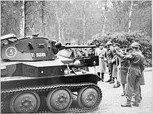 A group of soldiers, including several high-ranking officers, observe a Tetrarch light tank