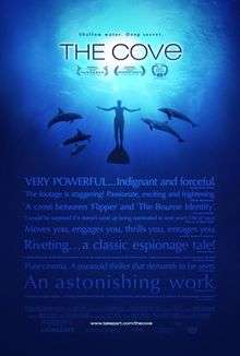 A man swimming underwater surrounded by five dolphins. Above is the title "The Cove" and the tagline "Shallow Water, Deep Secret". Below is a group of quotes from film critics giving praise to the film, with the credits of the film at the bottom.