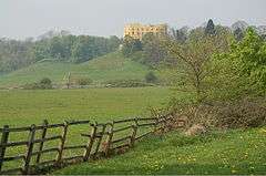 view of Stoke Park showing a broken fence in the foreground, with the Dower House and woodland on the skyline