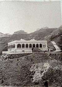 b/w image of a lone single-storey white stone building with arched balcony set in a hill