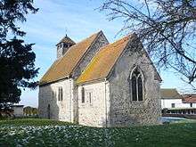 A flint church with red tiled roofs and a bellcote at the far end