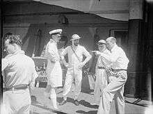 group shot of three men in naval uniform and one man in civilian dress talking to them