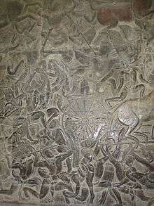 A black stone relief depicting a number of men wearing a crown and a dhoti, fighting with spears, swords and bows. A chariot with half the horse out of the frame is seen in the middle.