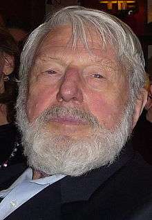 A headshot of a caucasian man with grey hair and a bushy grey beard.