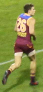 A man in a maroon football jersey wearing number 26 runs on grass.