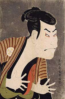 Colour print of a colourfully made-up Japanese actor making a bold expression with his fingers extended, facing right.