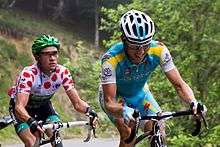 Thomas Voeckler wearing a white jersey with red polka dots, following Fredrik Kessiakoff as they ride up an incline.