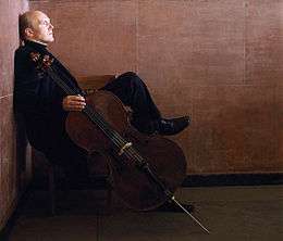 A man sitting in a chair, at rest, holding a cello at his side
