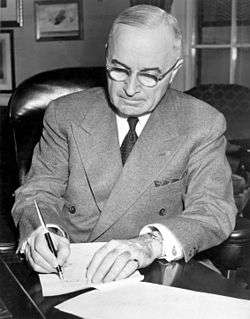 Man in gray suit and glasses signing a document