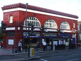 A red-bricked building with a rectangular, dark blue sign reading "TUFNELL PARK STATION" in white letters all under a blue sky with white clouds