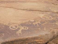 A sandstone slab in horizontal position, cracked in about half. The front piece features engravings of two antelopes. Four circles overlay the slab, two attached to the left antelope which probably depicts a Kudu, and two near the left antelope.