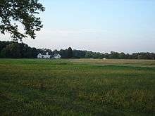 View across a field to a large white building and woods