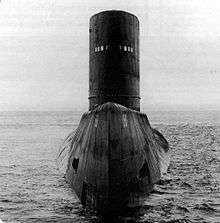 Large submarine surface displaying its bow, upper deck, and large conning tower.