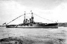 A large gray battleship sits in harbor