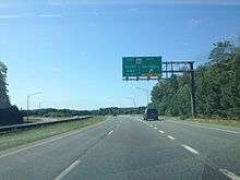 A four lane asphalt road with a grassy median approaching an interchange. A green overhead sign reads MD 90 east Ocean City 1/4 mile west Salisbury exit only.