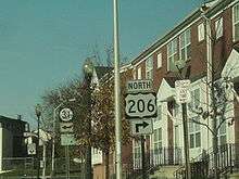 A street in an urban area with a sign reading north U.S. Route 206 right in the foreground and a Route 31 left sign in the background
