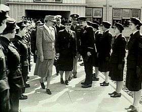 Two rows of women in dark military uniforms facing each other, with a number of other military personnel and one civilian walking between them