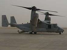  A side view of an MV-22 resting on sandy ground with its ramp lowered.