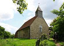 A small stone church with a red tiled roof and a wooden bellcote