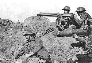 Four men in a barren landscape with a tripod-mounted machine gun