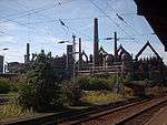 View from a train of numerous smoke stacks, tanks and pipes.
