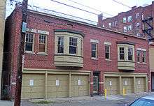 A two-story flat-roofed brick building on a city street. It has two triple garages at street level separated by an entrance, and two bay windows in the second separated by two regular windows.