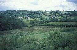 Green rolling hills with a cluster of houses and a church left of centre.