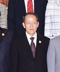 a nearly bald man, wearing glasses, a suit and a purple tie