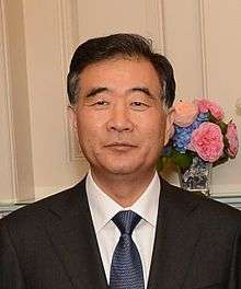 a man with a wavy haircut, wearing a white shirt, a suit and a blue tie