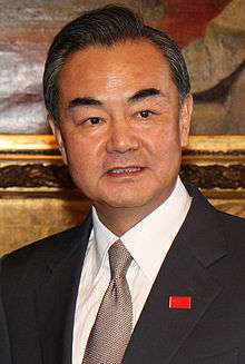 a man, wearing a suit and a black-greenish tie with a People's Republic of China badge on the right side of his suit