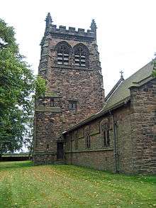 A castellated tower with the nave of the church to the right; a tree is to the left and the churchyard is grassed