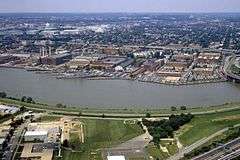Aerial photograph of the Washington Navy Yard with a destroyer at dock, the Anacostia River in the foreground and Capitol Hill in the background.