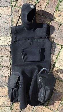 Sleeveless tunic in thin but abrasion resistant neoprene, with integral hood, two cargo pochets on the sides of the thighs, cross-chest zip closure, front pocket on the torso and opening for access to a dry-suit inflation valve. The tunic is suitable for wearing over most one-piece wetsuits for extra insulation, but mainly to support the cargo pockets and hood.